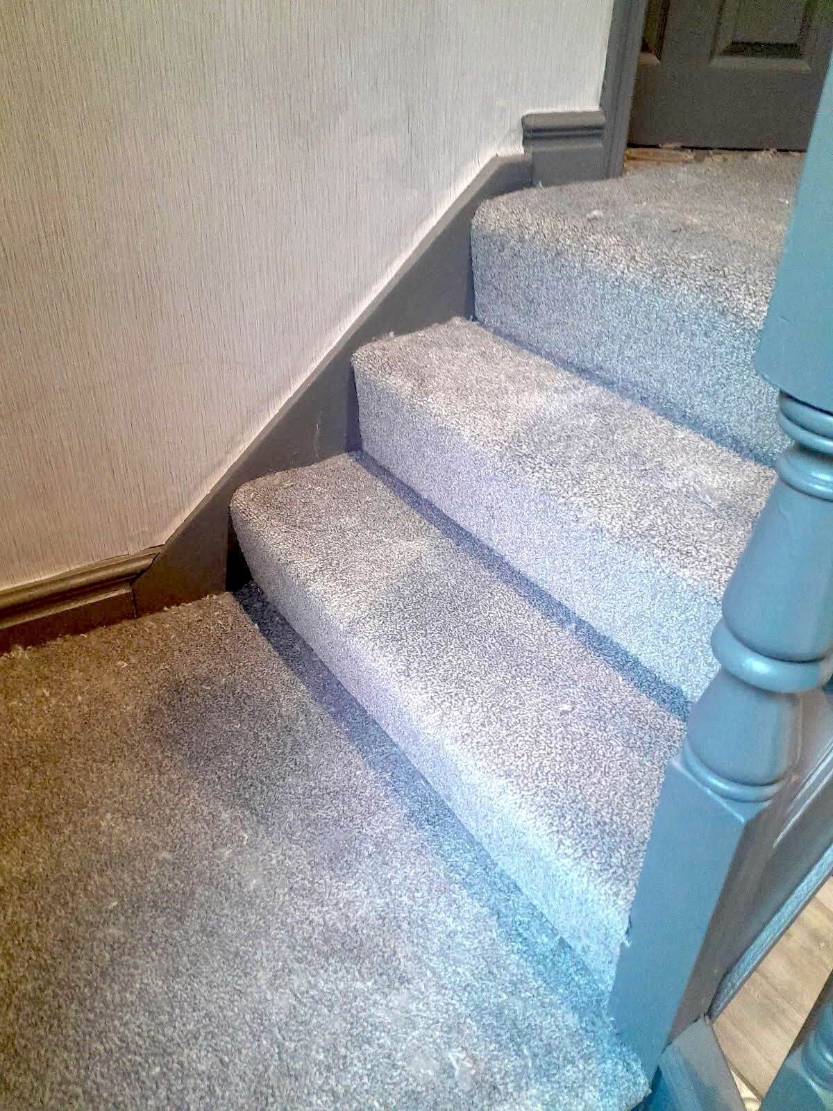 Gray carpeted stairs with a painted gray banister against a light gray wall.