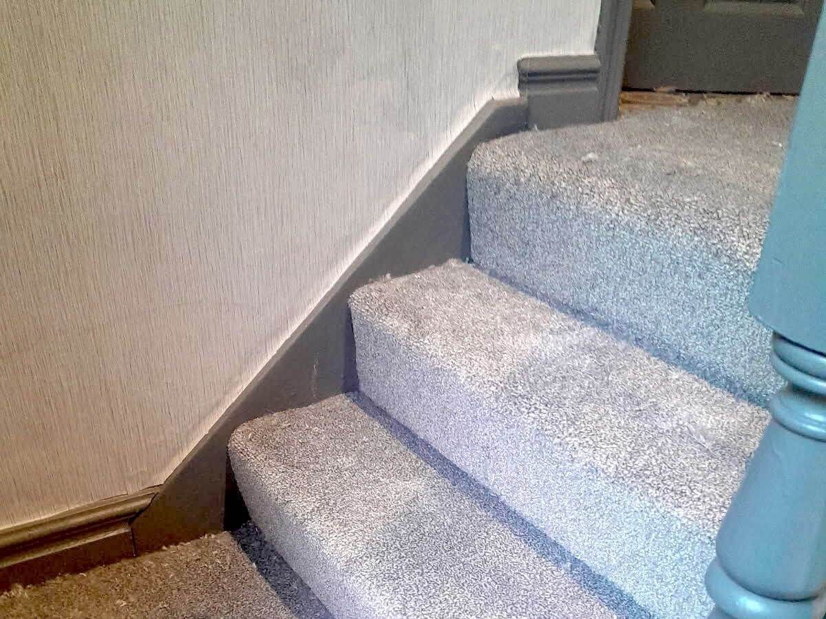 Gray carpeted stairs with gray painted trim and a section of a blue banister.