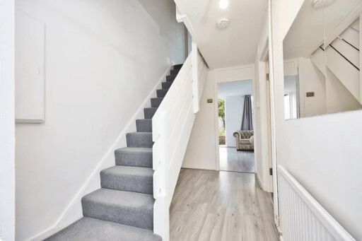 Hallway with gray carpeted stairs, white walls and wood-look flooring, leading to a room.