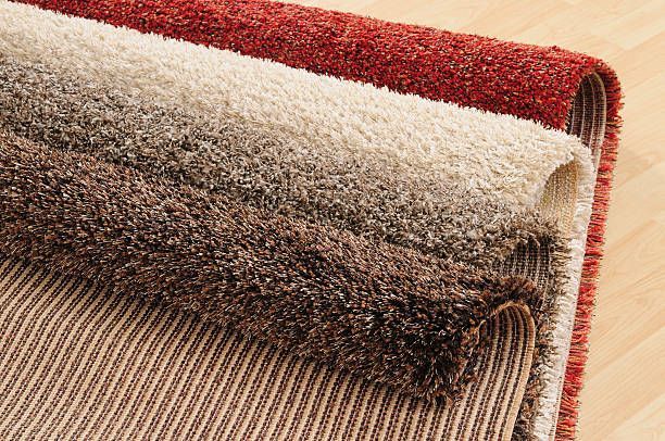 Three rolled-up rugs in red, tan/brown, and brown shades, stacked on top of one another.