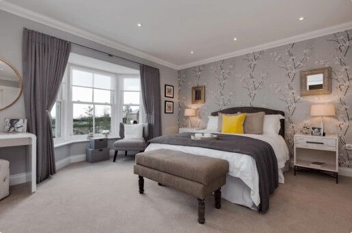 Bedroom with gray walls, bay window, bed, bench, and side tables.