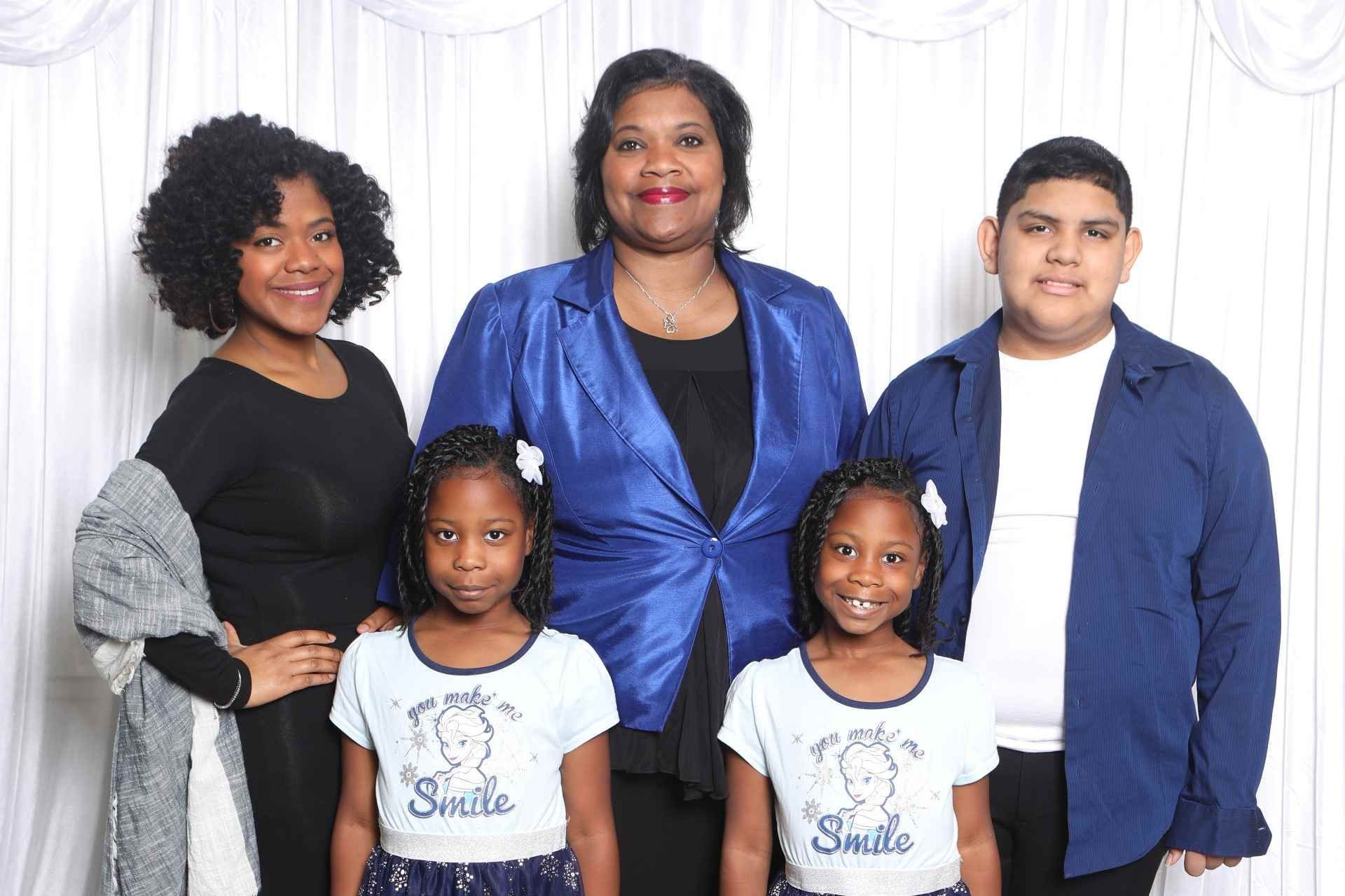 Family of five posing together in coordinated blue and black outfits against a white backdrop