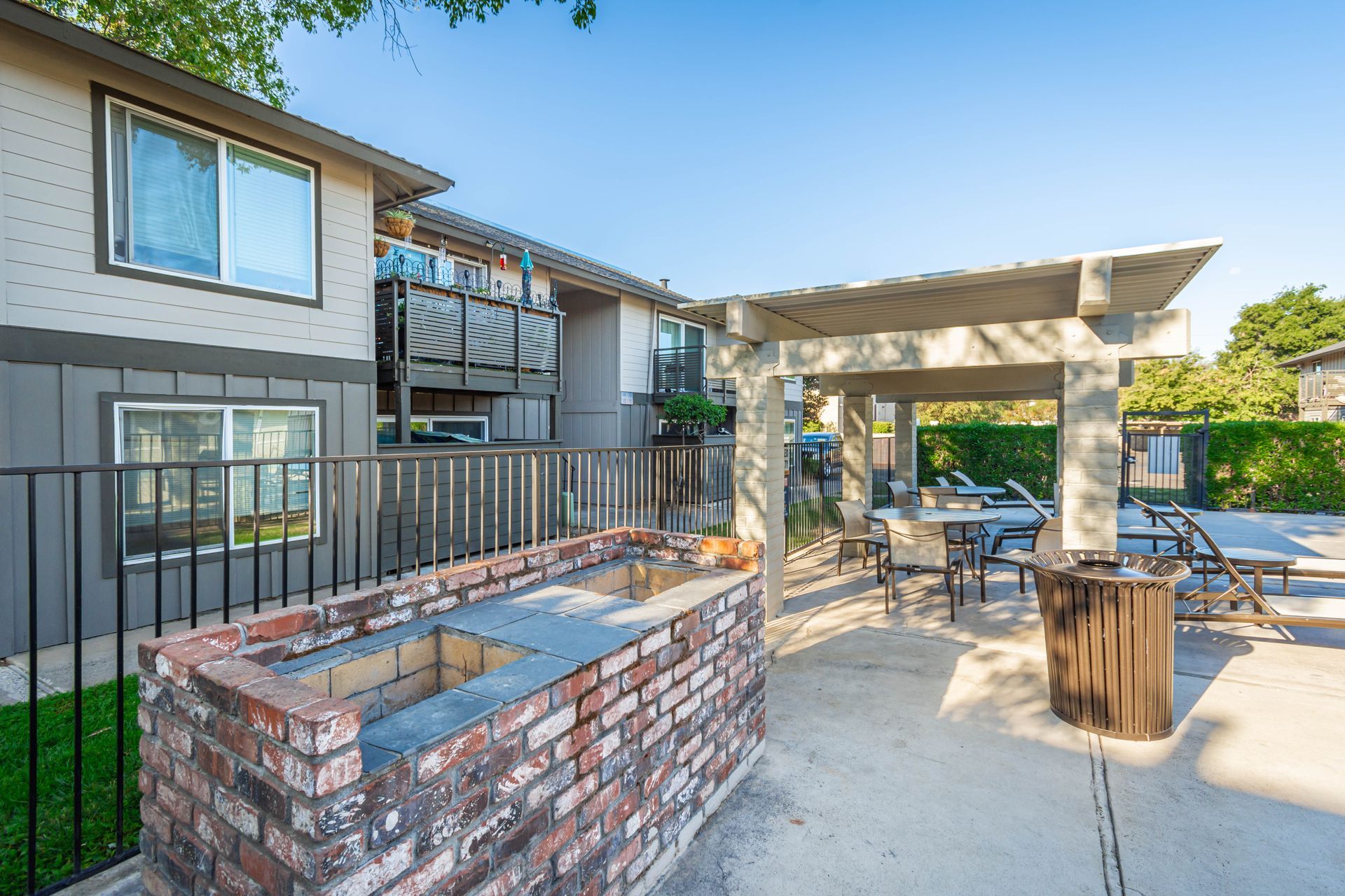 A brick grill is sitting under a pergola in front of a building.