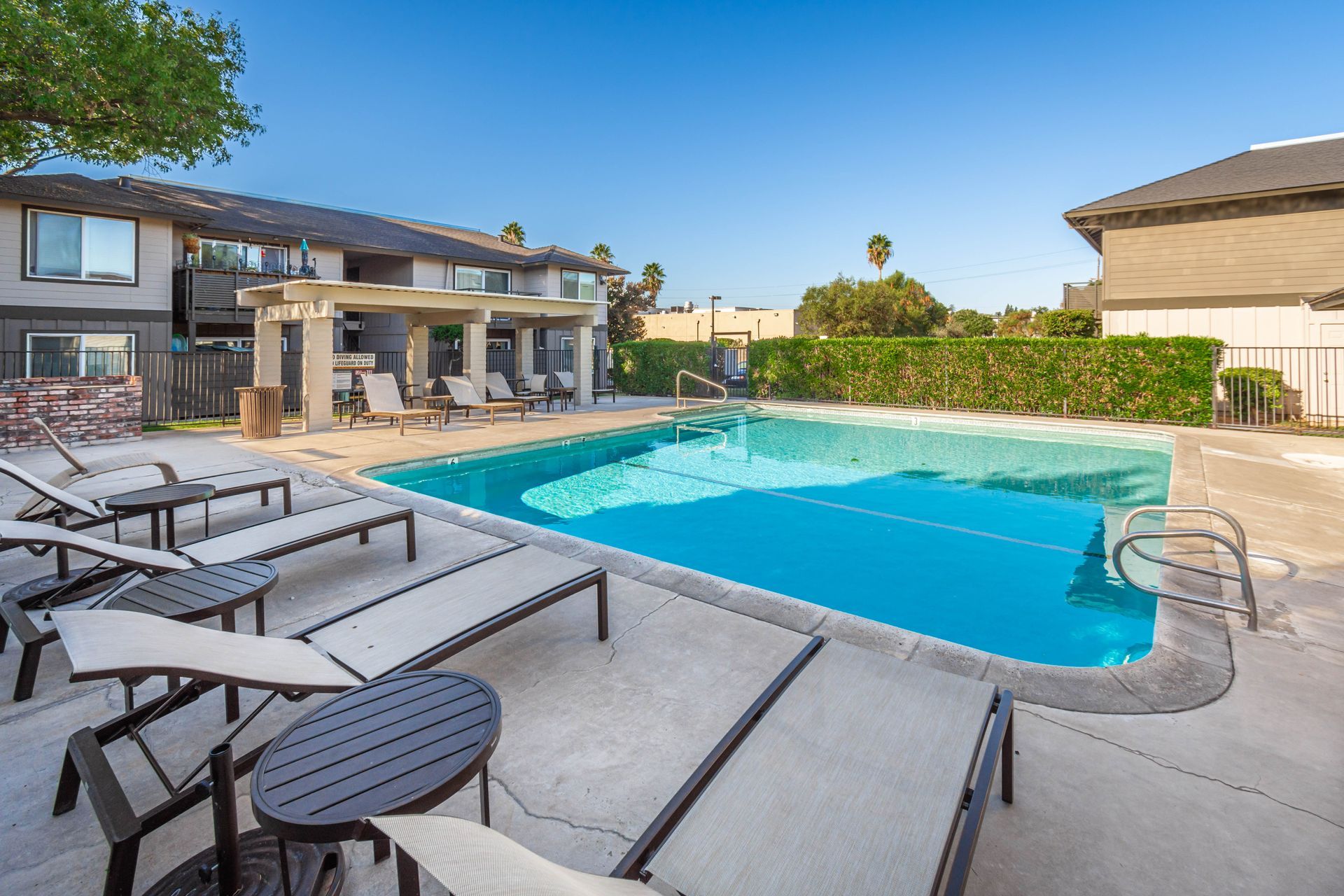 A large swimming pool surrounded by lounge chairs and tables in front of a building.