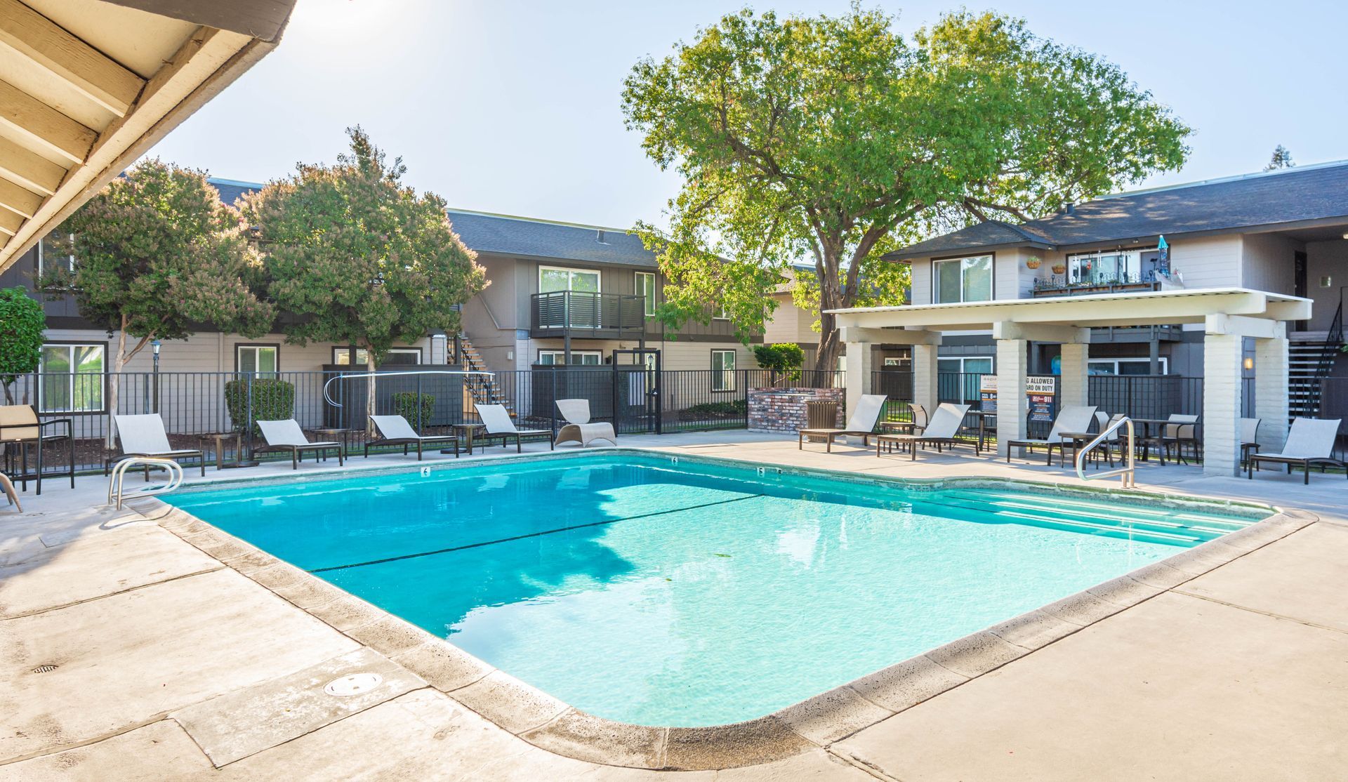 A large swimming pool surrounded by chairs and umbrellas in front of a building.