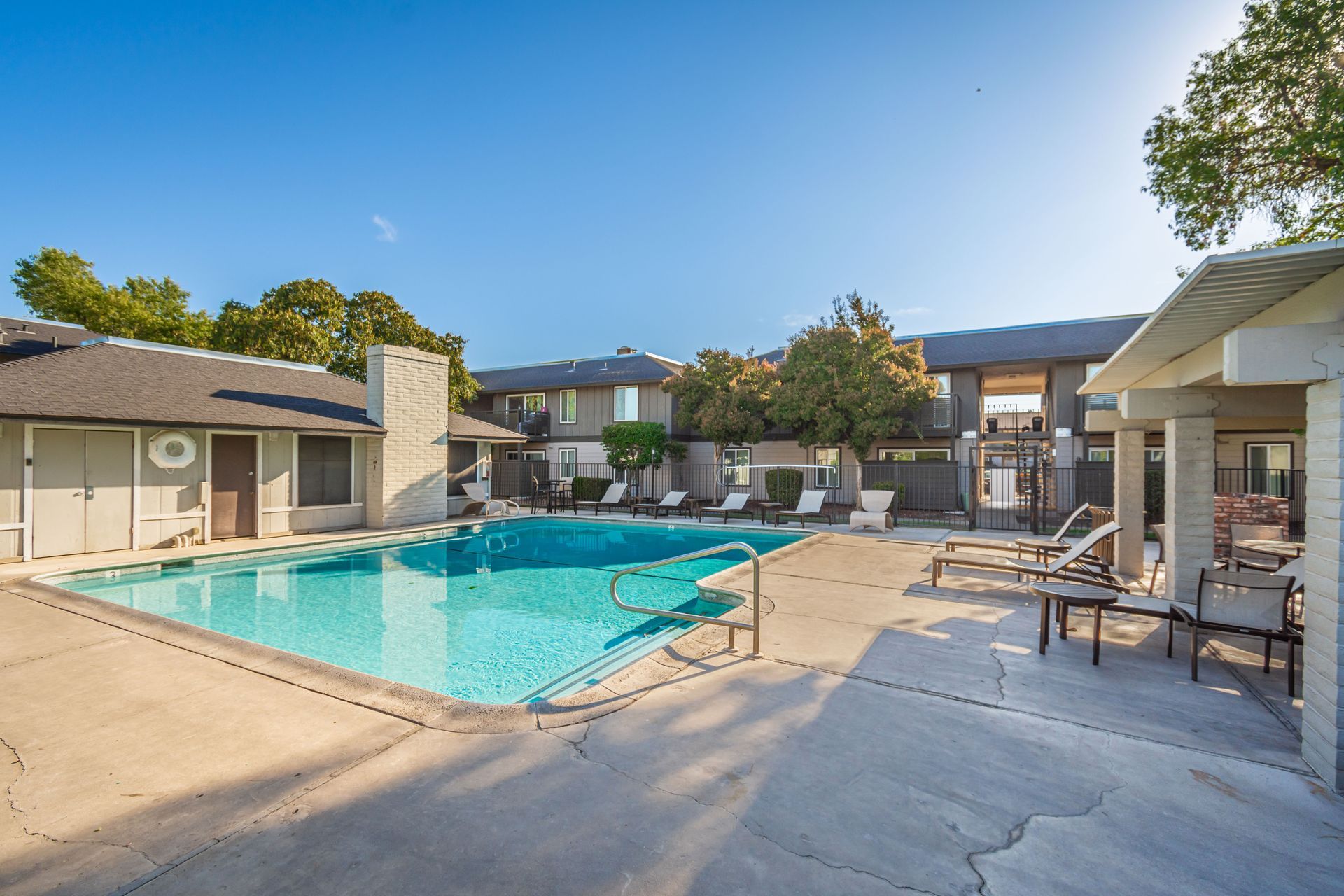 A large swimming pool is surrounded by chairs and buildings.
