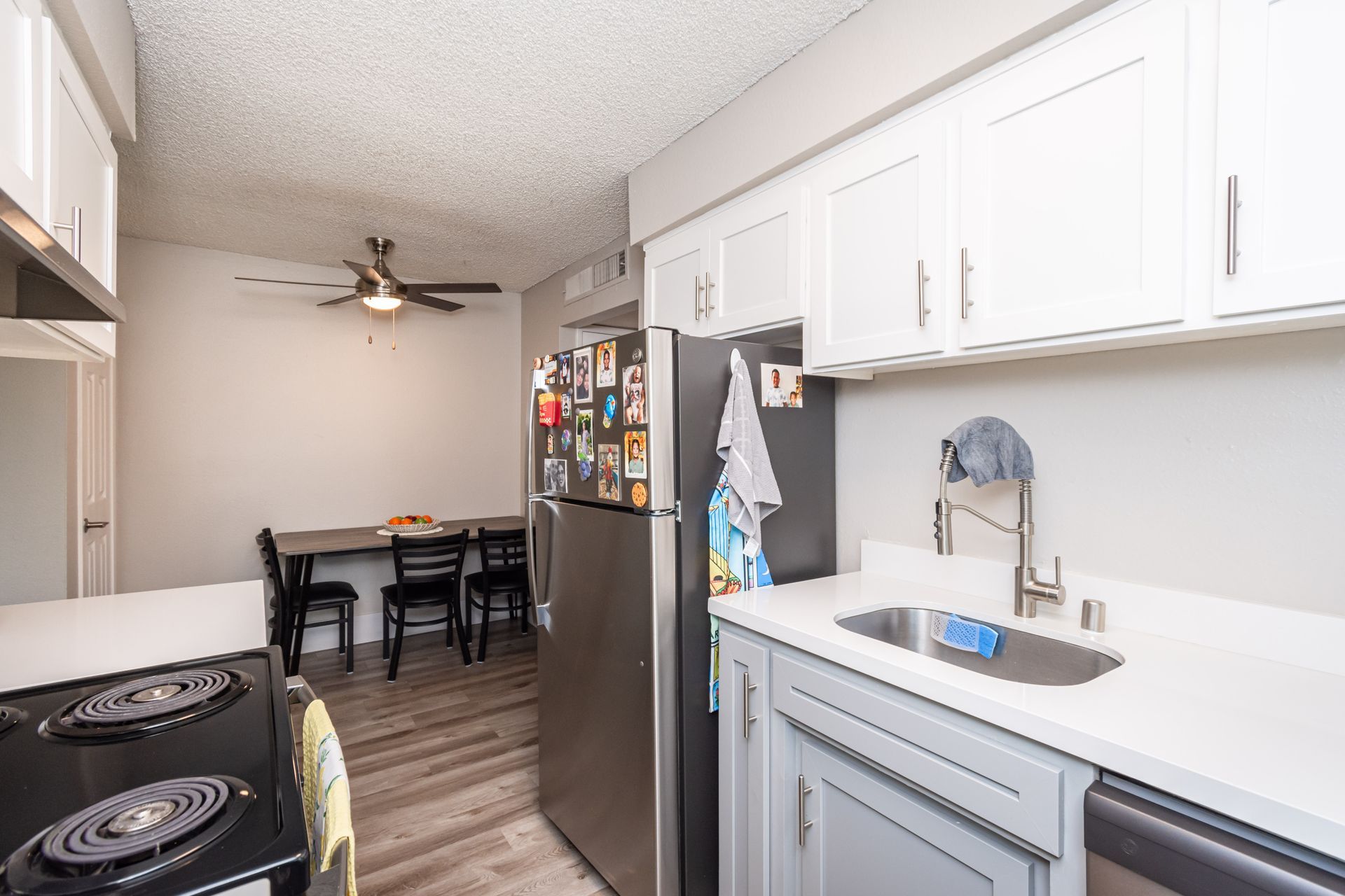 A kitchen with a sink , stove , refrigerator and ceiling fan.