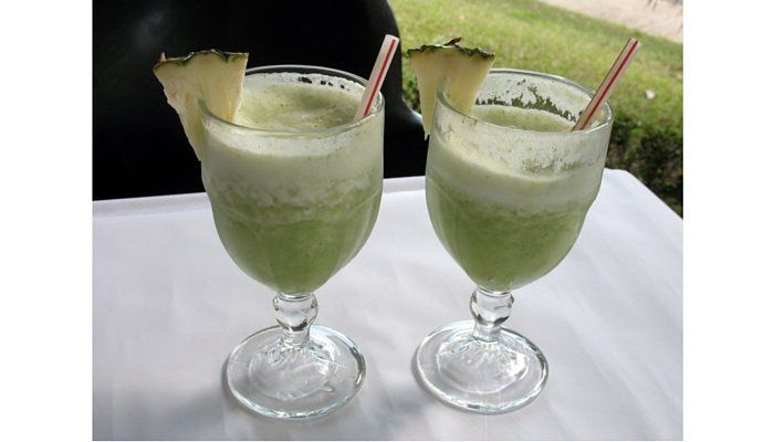 2 copas de jugo verde con pitillos y trocitos de piña