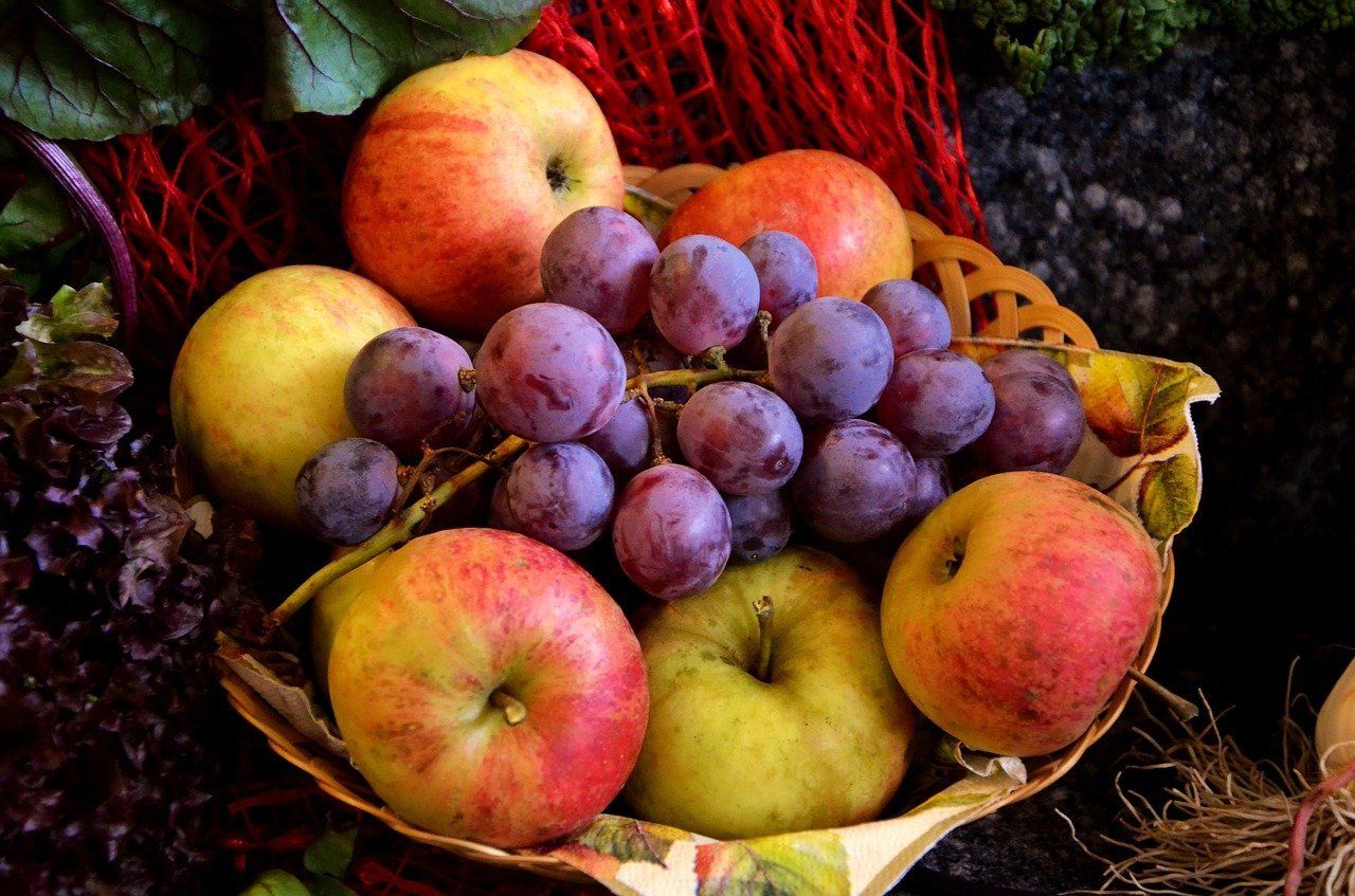 Canasta con manzanas y un racimo de uvas moradas