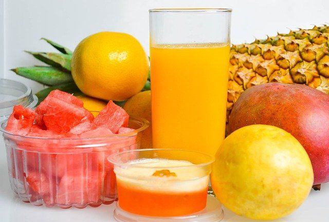 vaso de jugo amarillo entre frutas como piña, sandía y naranja