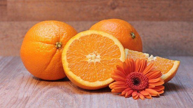 2 naranjas completas y una cortada con una flor danajo