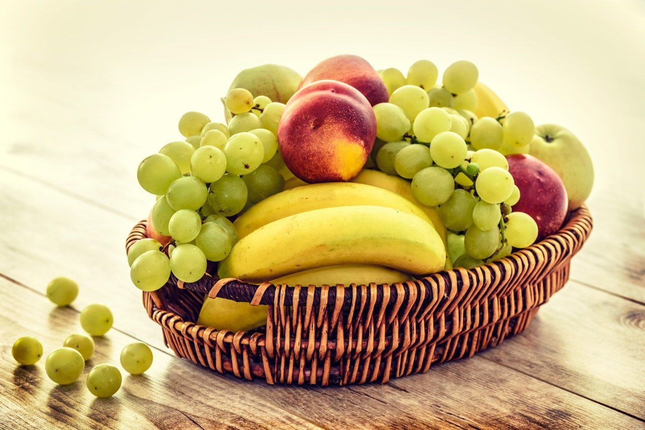Canasta de frutas con: uvas, duraznos y bananos