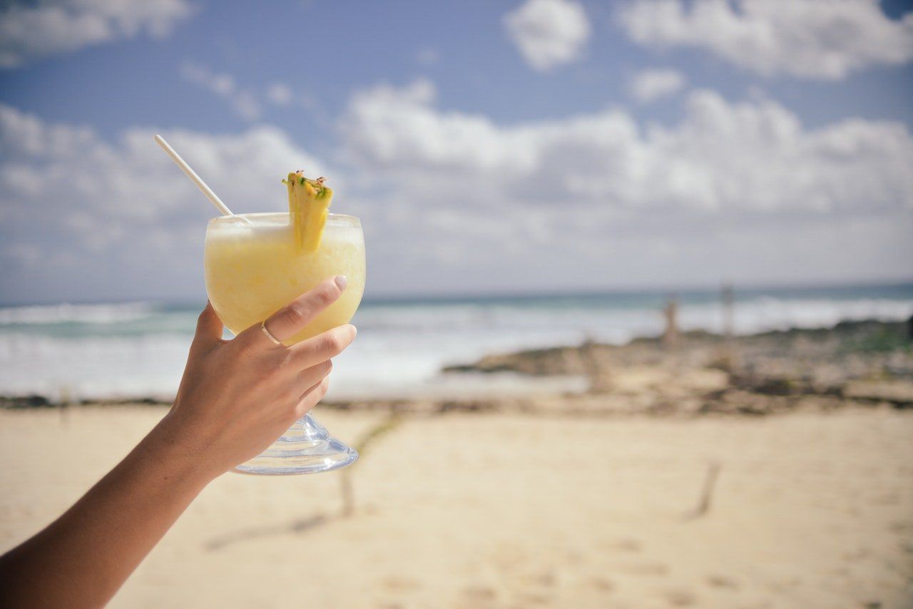 Copa de jugo de piña en una mano con playa al fondo