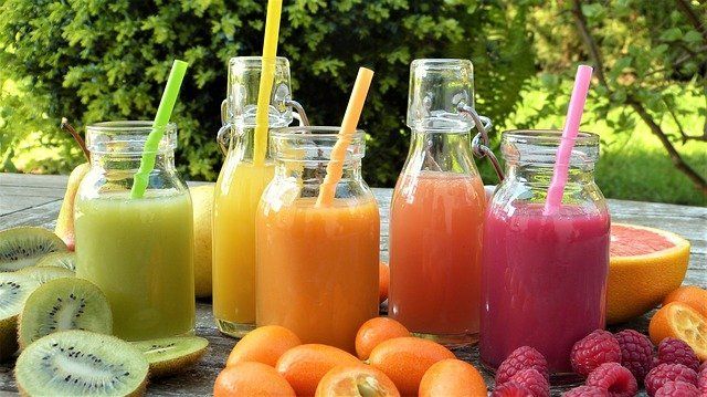 5 jarros con diferentes jugos en una mesa entre frutas naturales