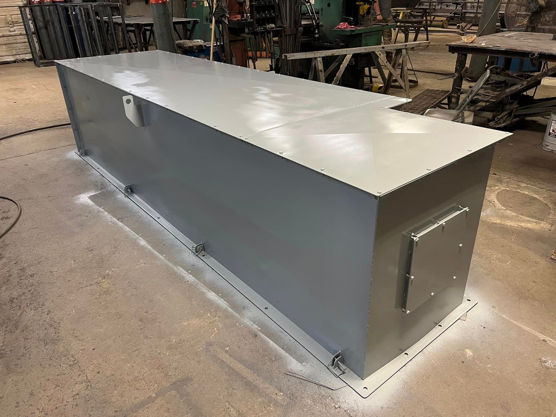 A large gray metal box is sitting on the floor in a factory.