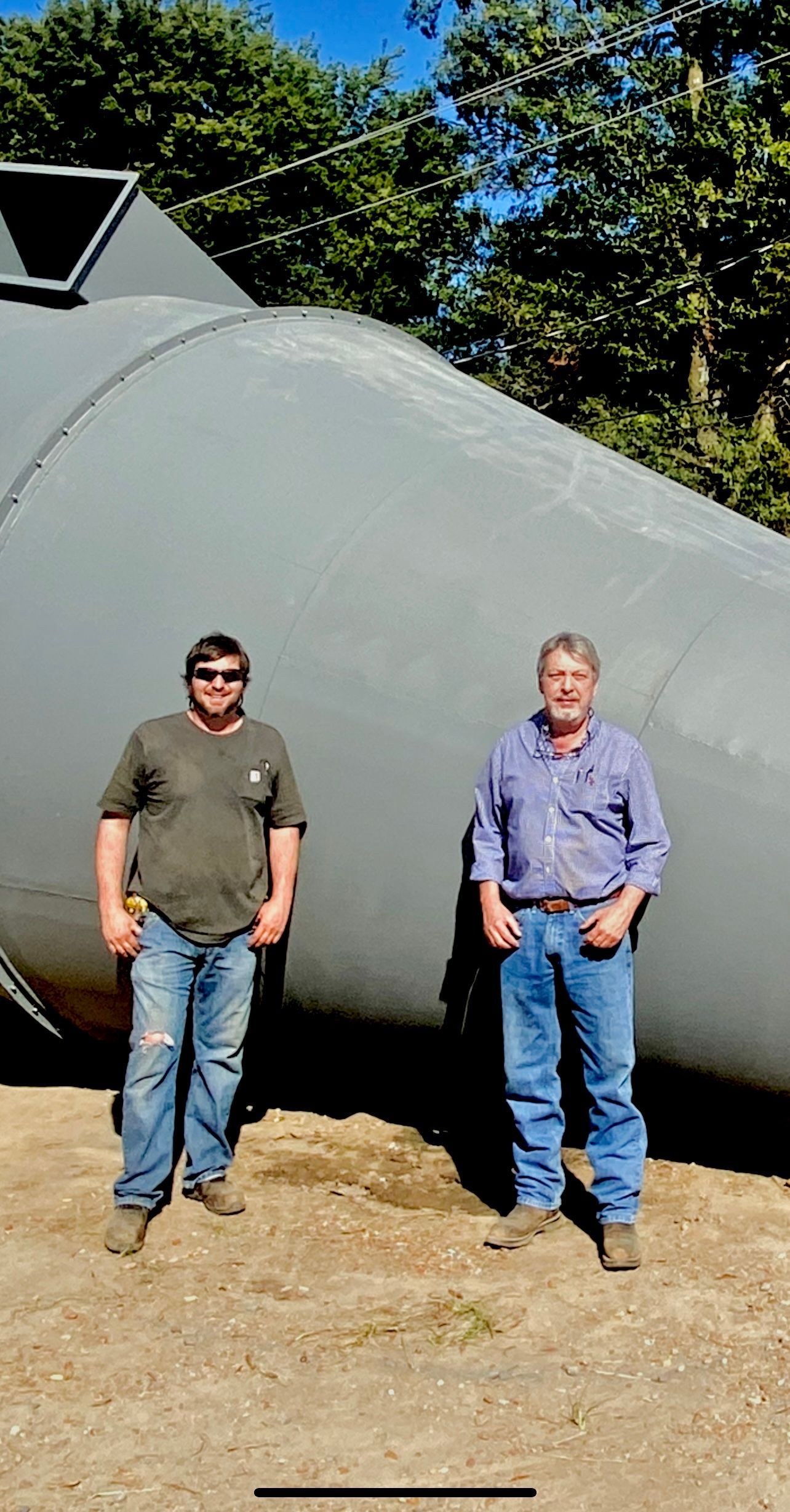 Two men are standing in front of a large gray object.
