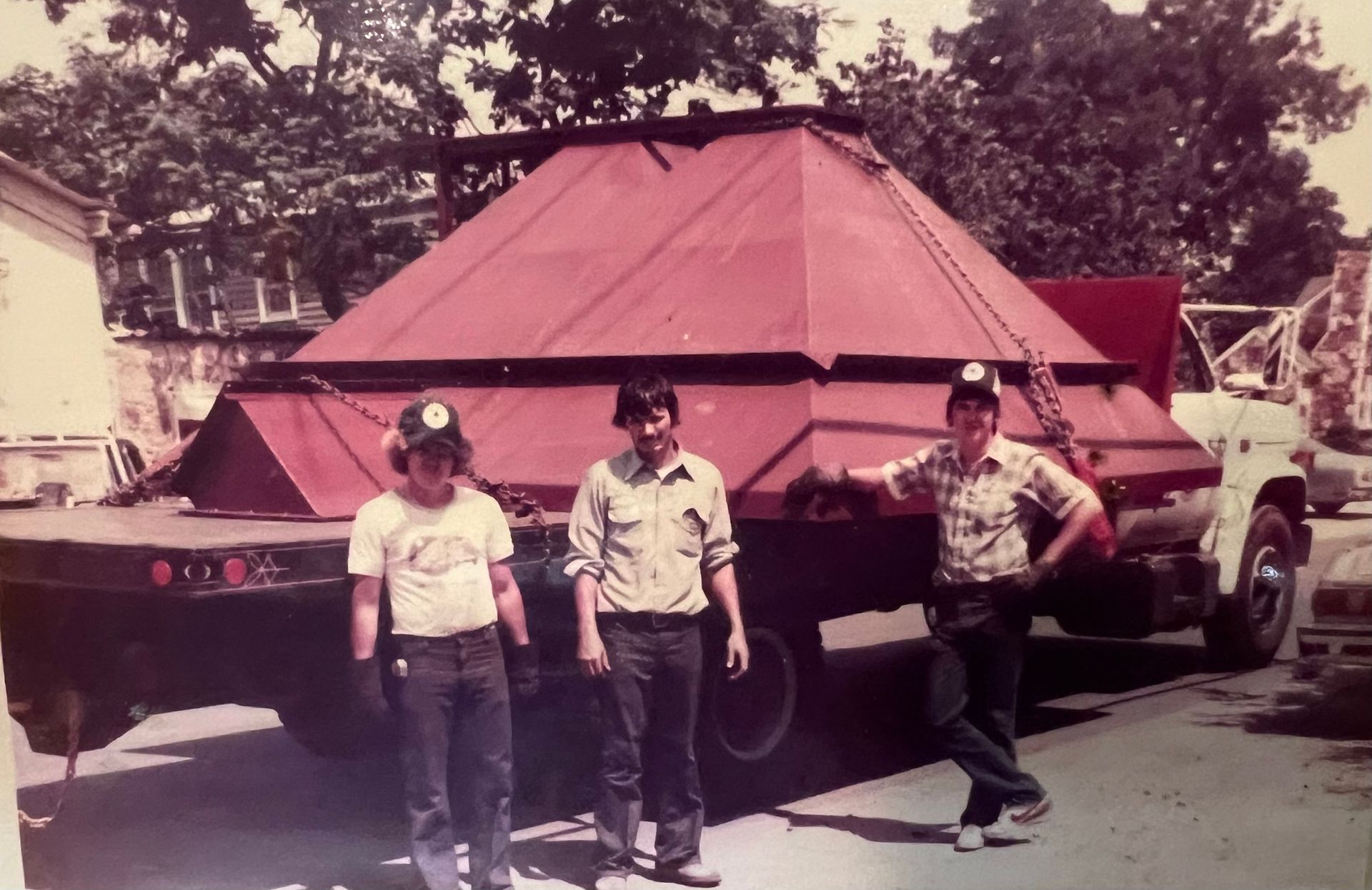 Three men are standing in front of a large red truck