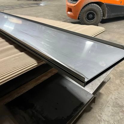 A forklift is driving past a stack of metal sheets.