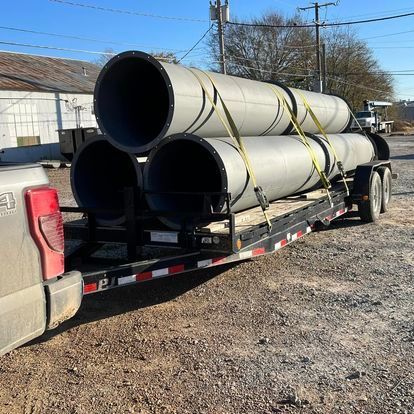 A truck is carrying three large pipes on a trailer.