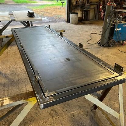 A metal door is sitting on top of a metal table in a garage.