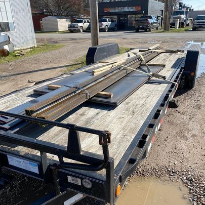 A trailer with a lot of metal pieces on it is parked on the side of the road.