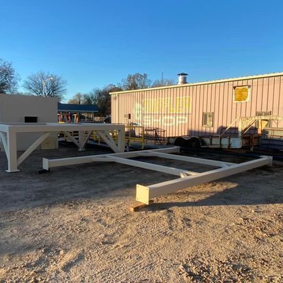 A large metal structure is sitting in the dirt in front of a building.