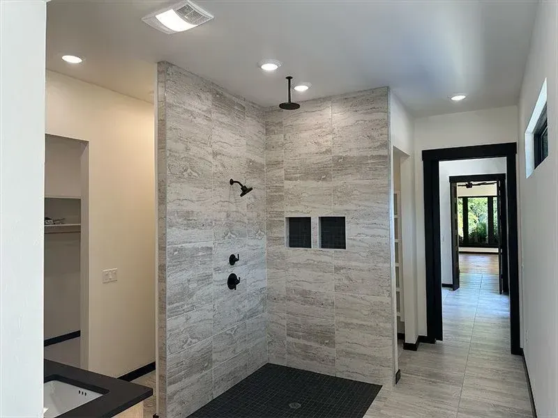 Modern bathroom featuring a walk-in shower with grey stone-look tiles, black fixtures, and a black pebble shower floor.