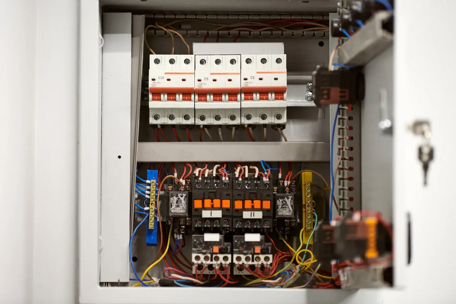 An open gray electrical panel containing several circuit breakers and relays connected by various colored wires.