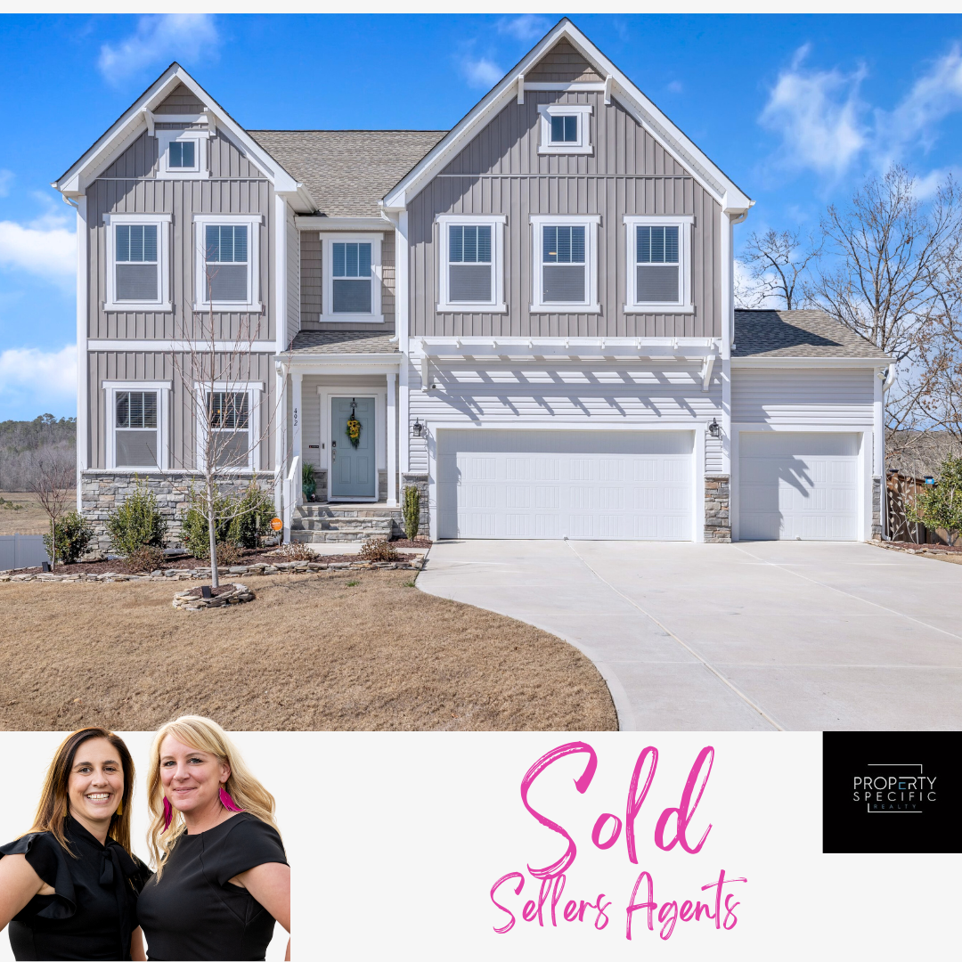 Two-story house with gray siding, white trim, and attached garage. Two real estate agents stand in front of
