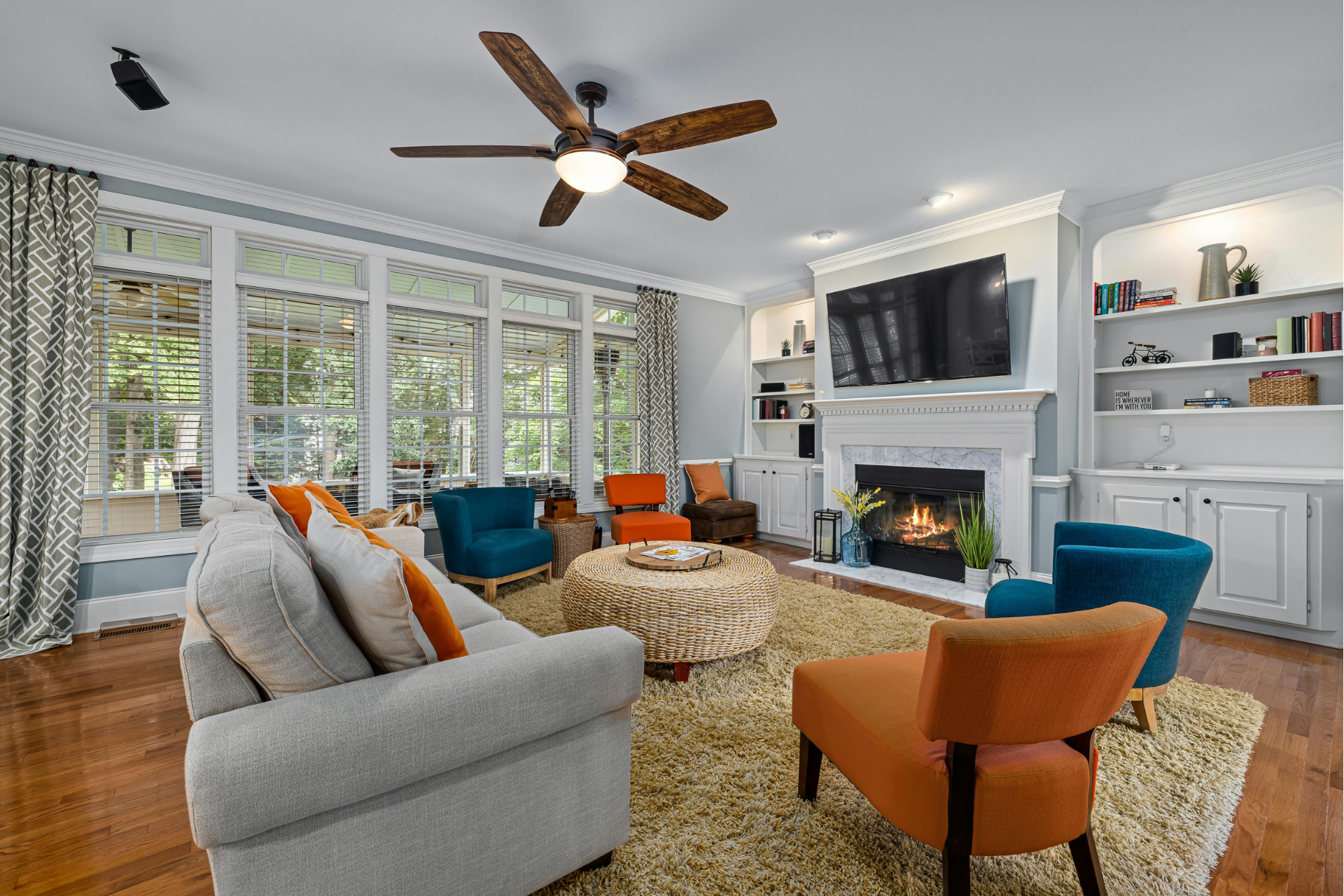 Living room with fireplace, windows, and colorful seating, including teal and orange chairs, plus a beige couch.