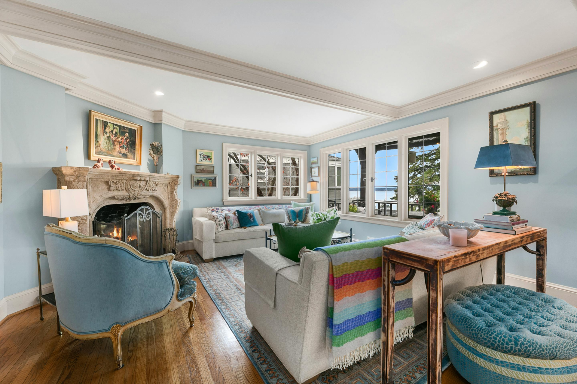 Living room with blue walls, ornate fireplace, white sofas, and lake view through windows.