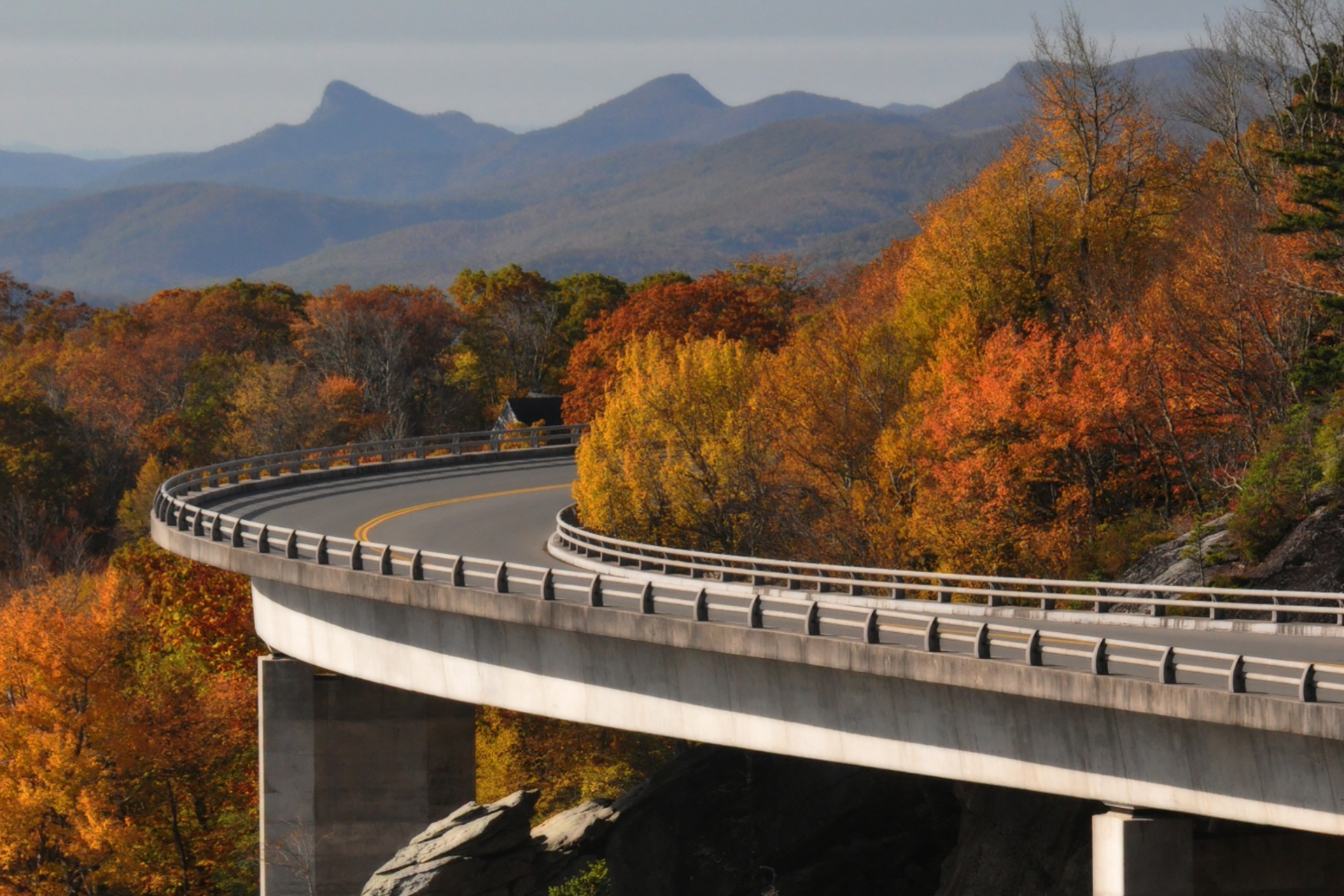Curving mountain highway in autumn; fall foliage, distant mountains, blue sky.