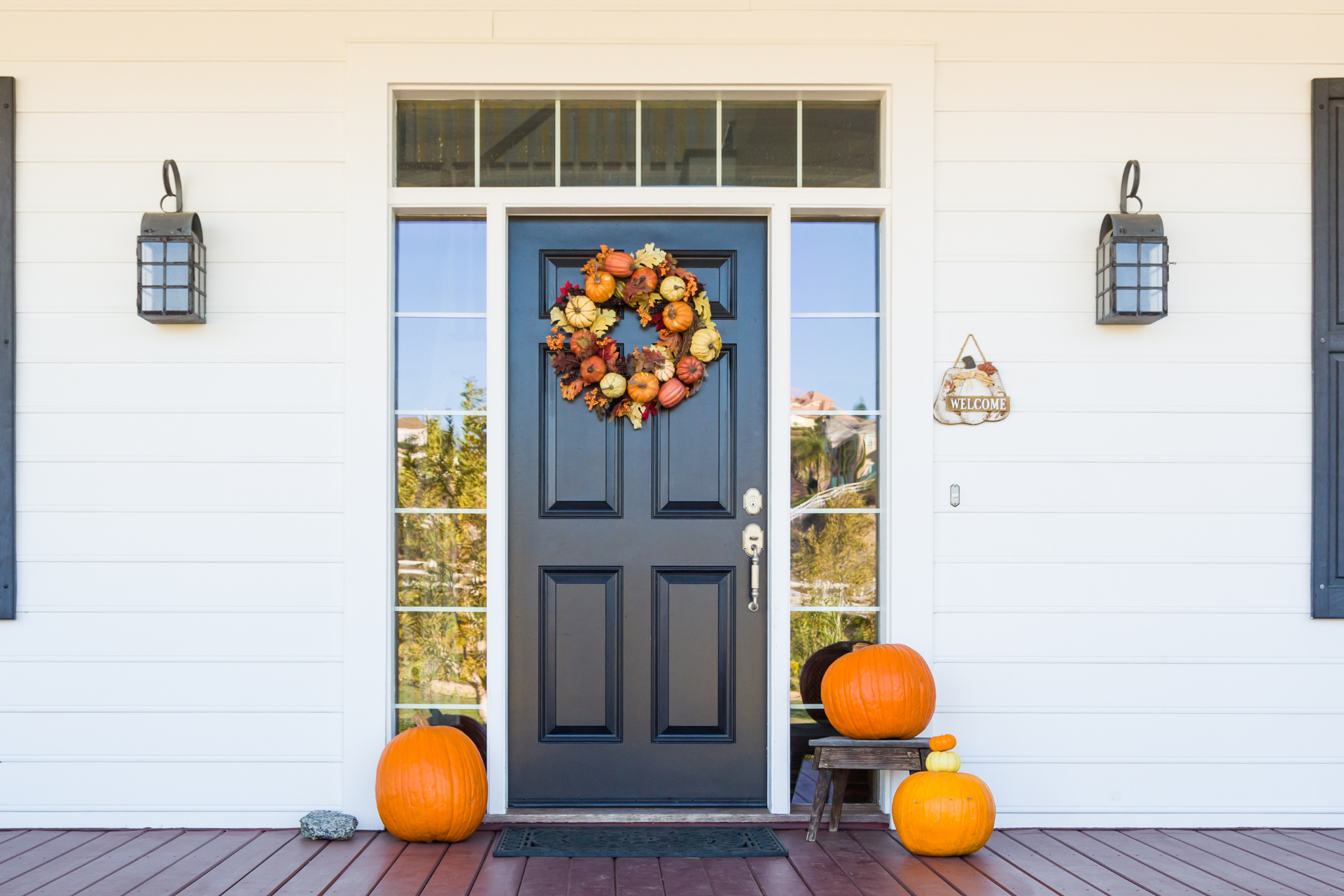 Fall-decorated front porch with pumpkins, mums, boots, and a rocking chair with a plaid pillow.