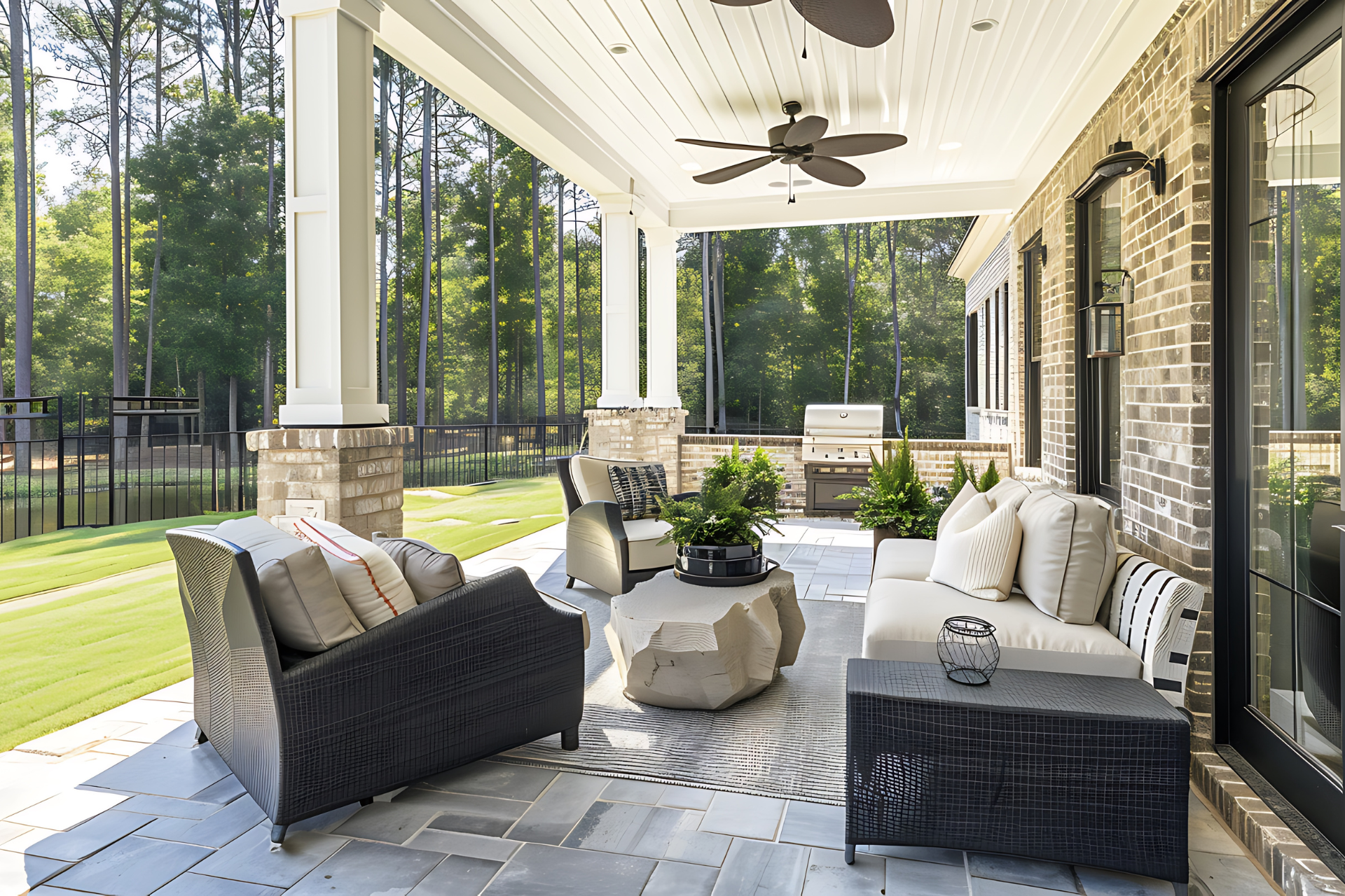 Covered patio with seating, brick columns, outdoor grill, and trees in the background.