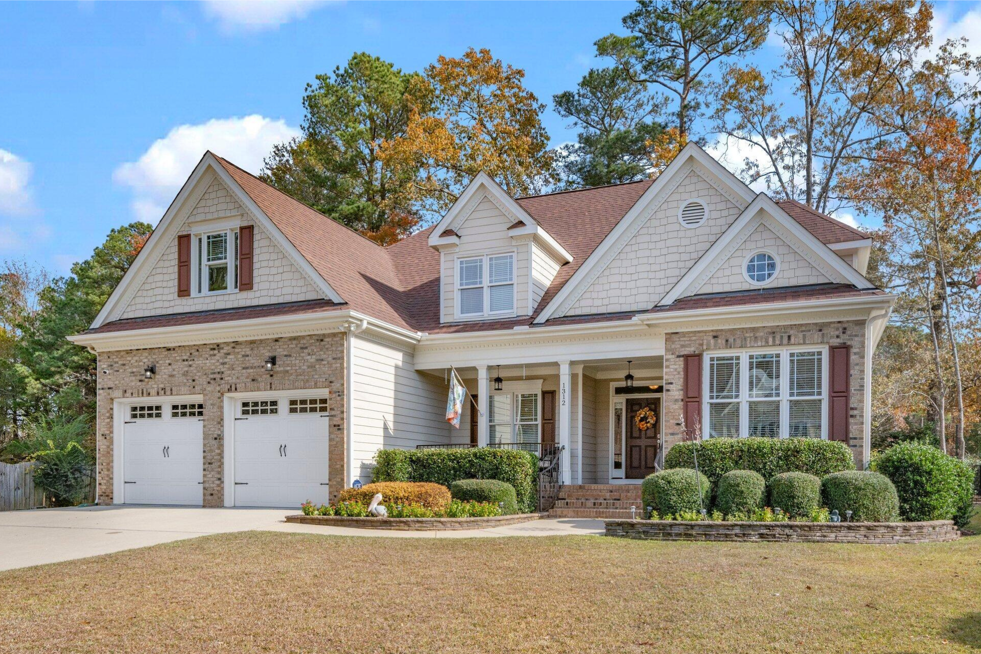 Curb appeal of a two-story beige and brick house with a brown roof and a green manicured lawn.