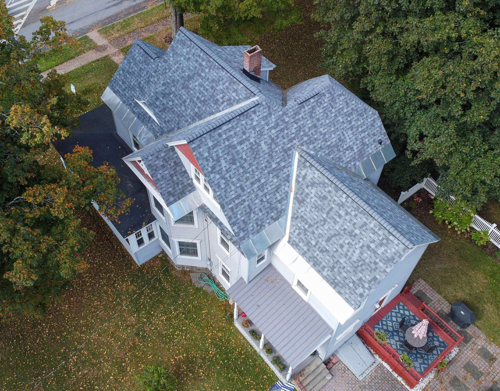 Aerial view of a gray house with a complex roof and surrounding trees on a grassy lot.