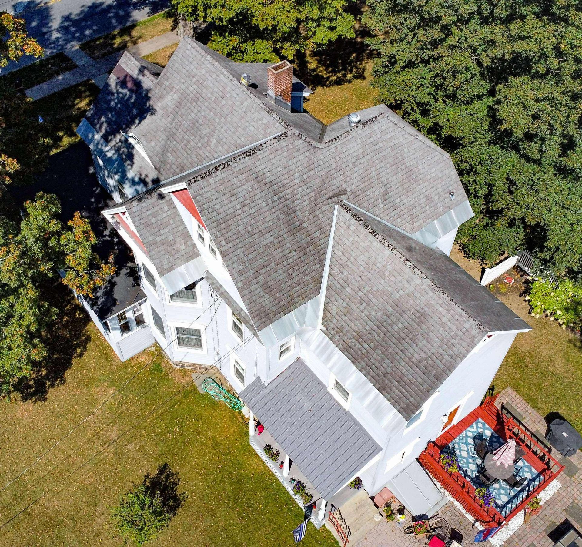 White house with gray roof surrounded by trees and grass, seen from above.