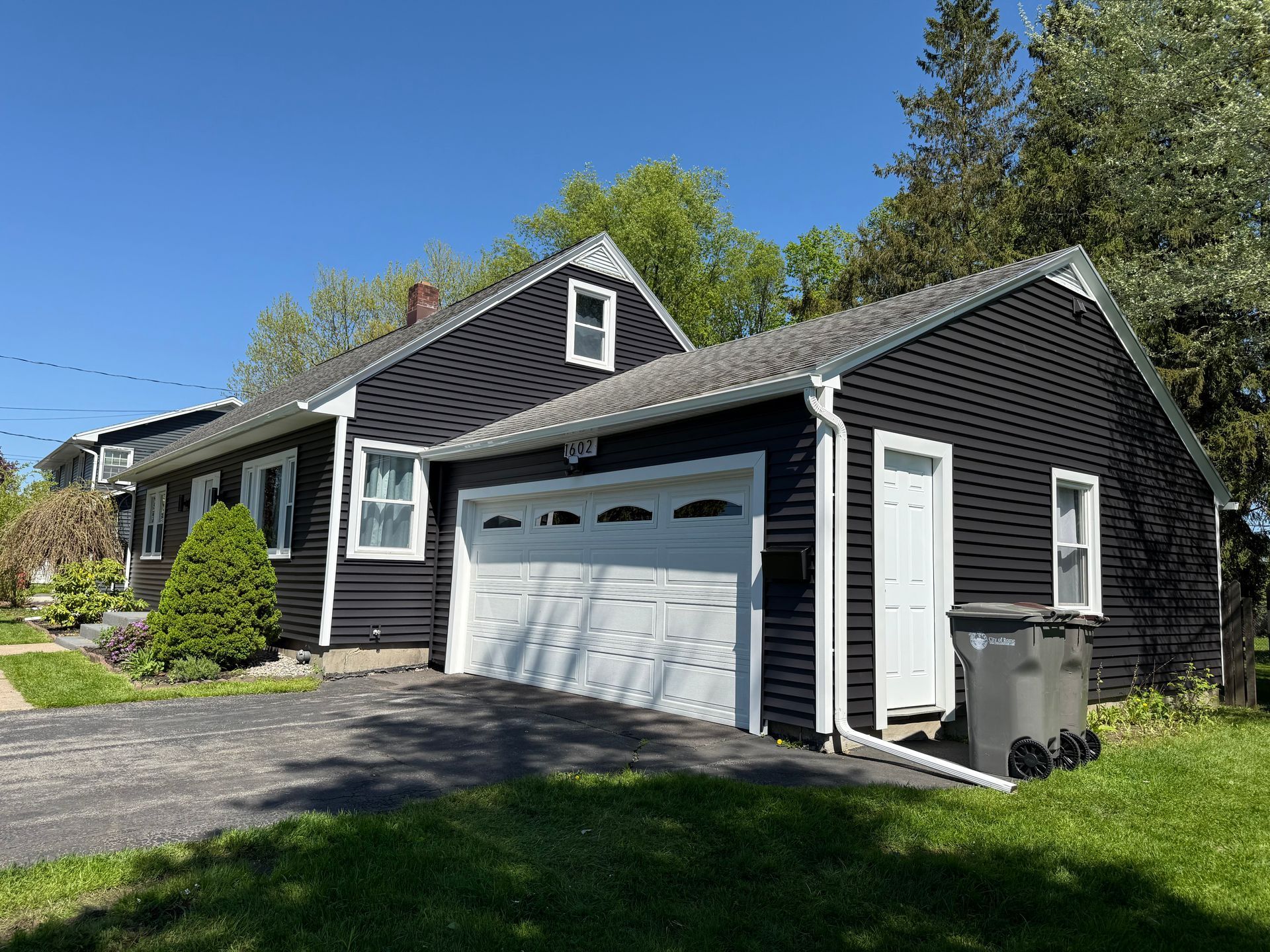A black house with a white garage door and a trash can in front of it