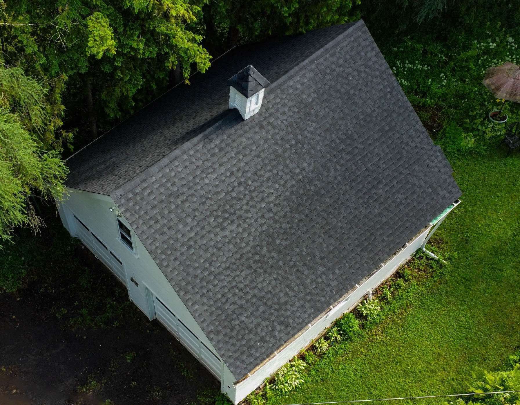 An aerial view of a white house with a black roof surrounded by trees