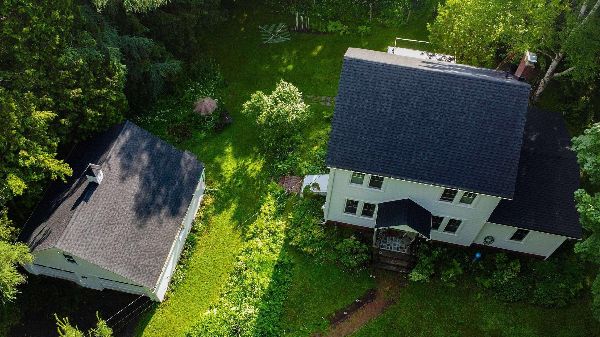 An aerial view of two houses in a lush green field surrounded by trees