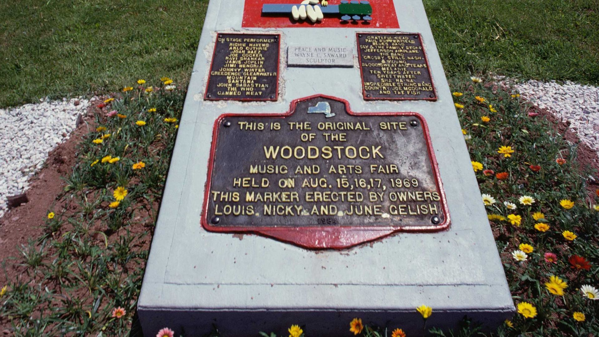 A large rock with a plaque on it is in the middle of a park next to a picnic table.