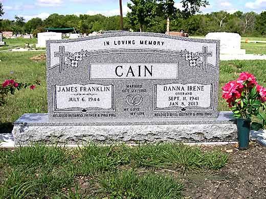 A gravestone for cain in a cemetery with flowers in front of it.