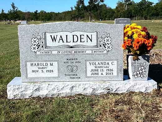 A gravestone for walden in a cemetery with flowers in a vase.