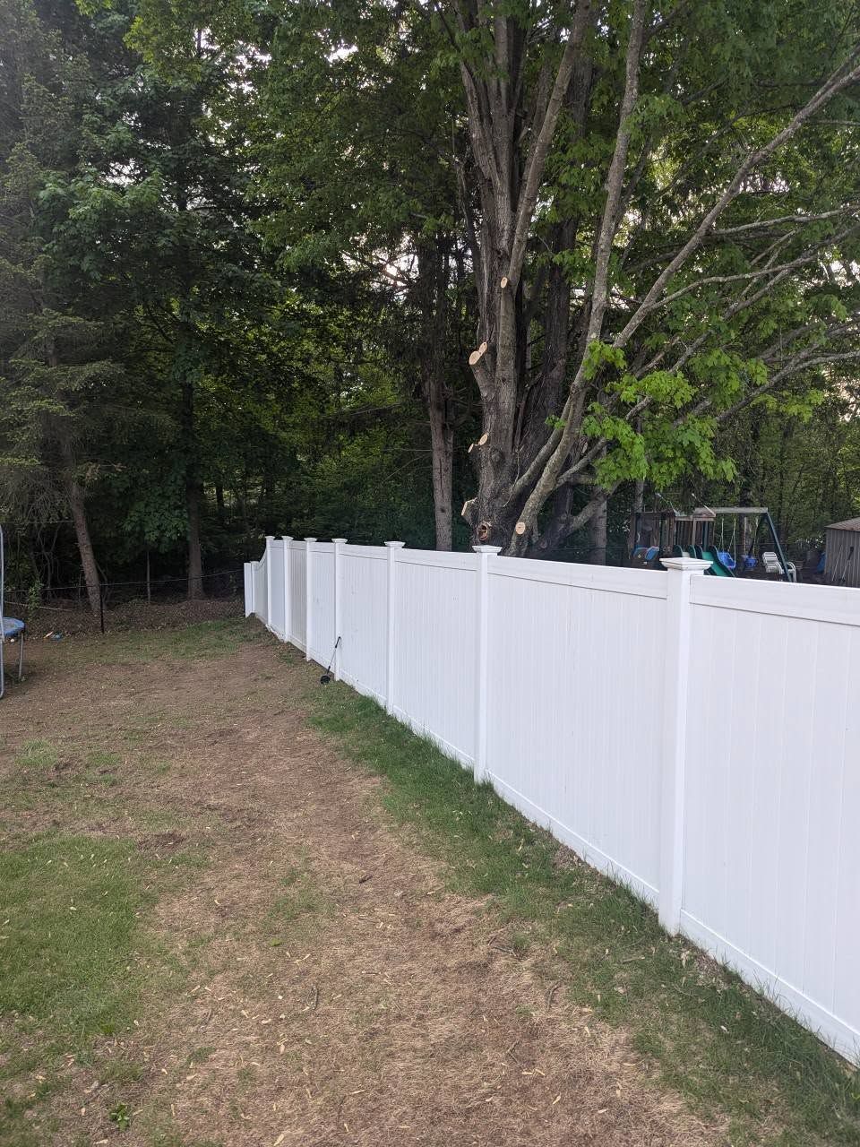 A white vinyl fence is surrounded by trees in a backyard.