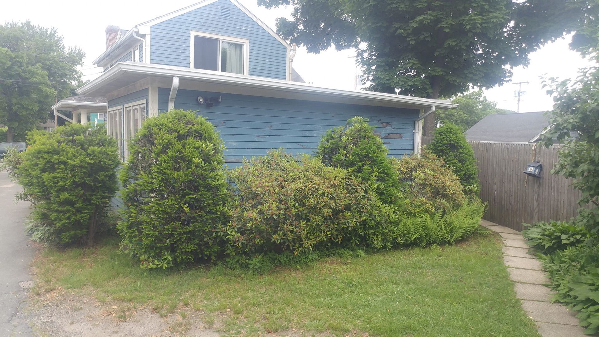 A blue house with a fence and bushes in front of it.