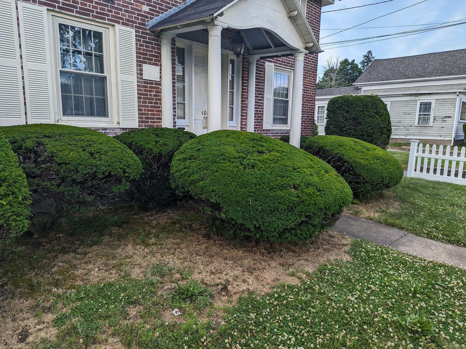 A brick house with a white picket fence and bushes in front of it.