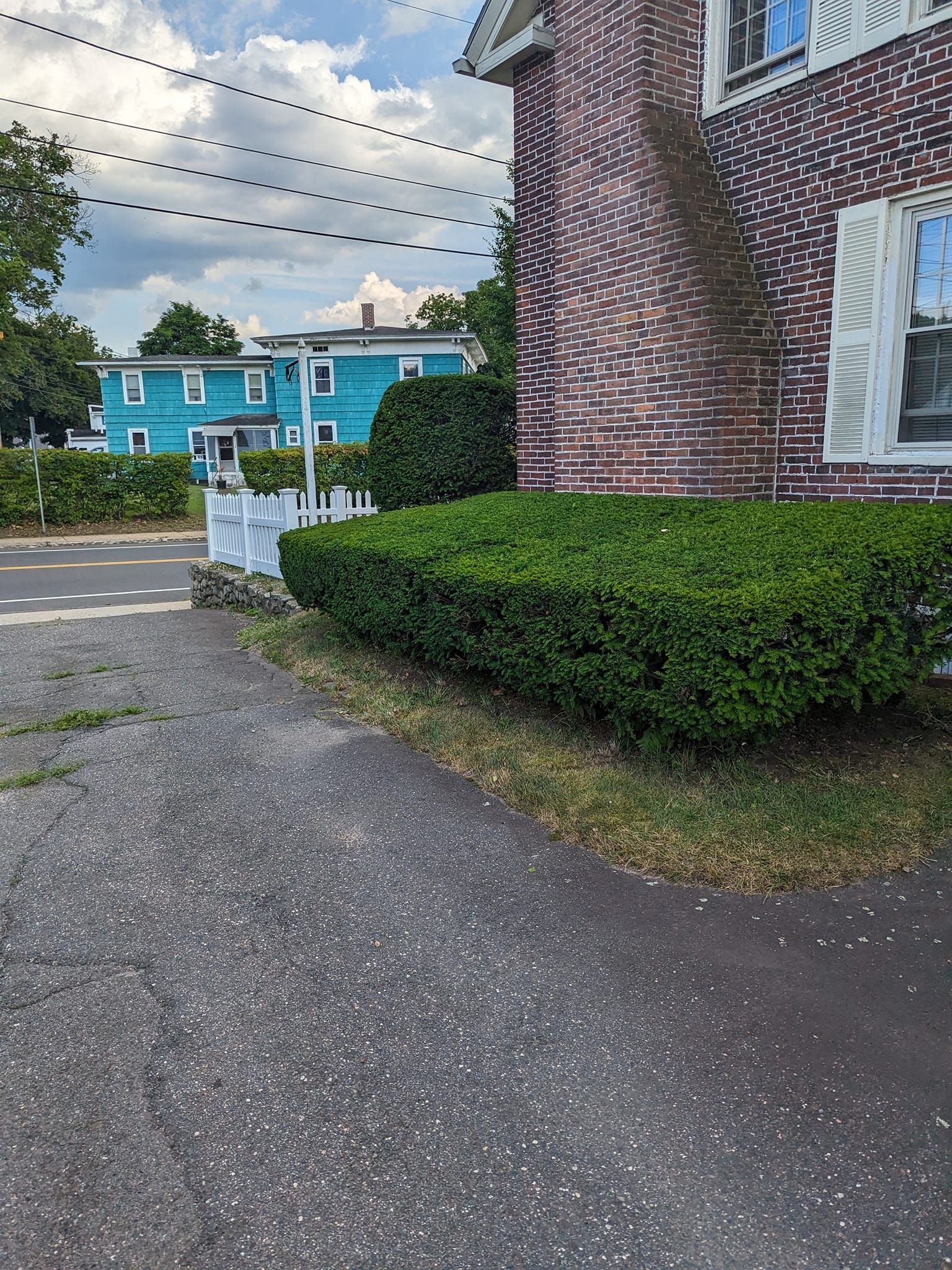 A brick house with a lot of bushes in front of it and a blue house in the background.