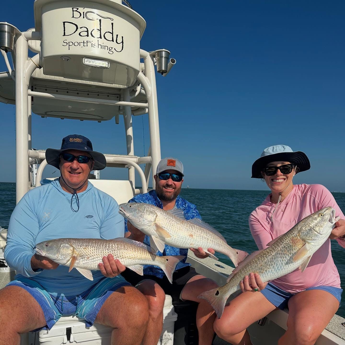 Two men and a woman are sitting on a boat holding fish.