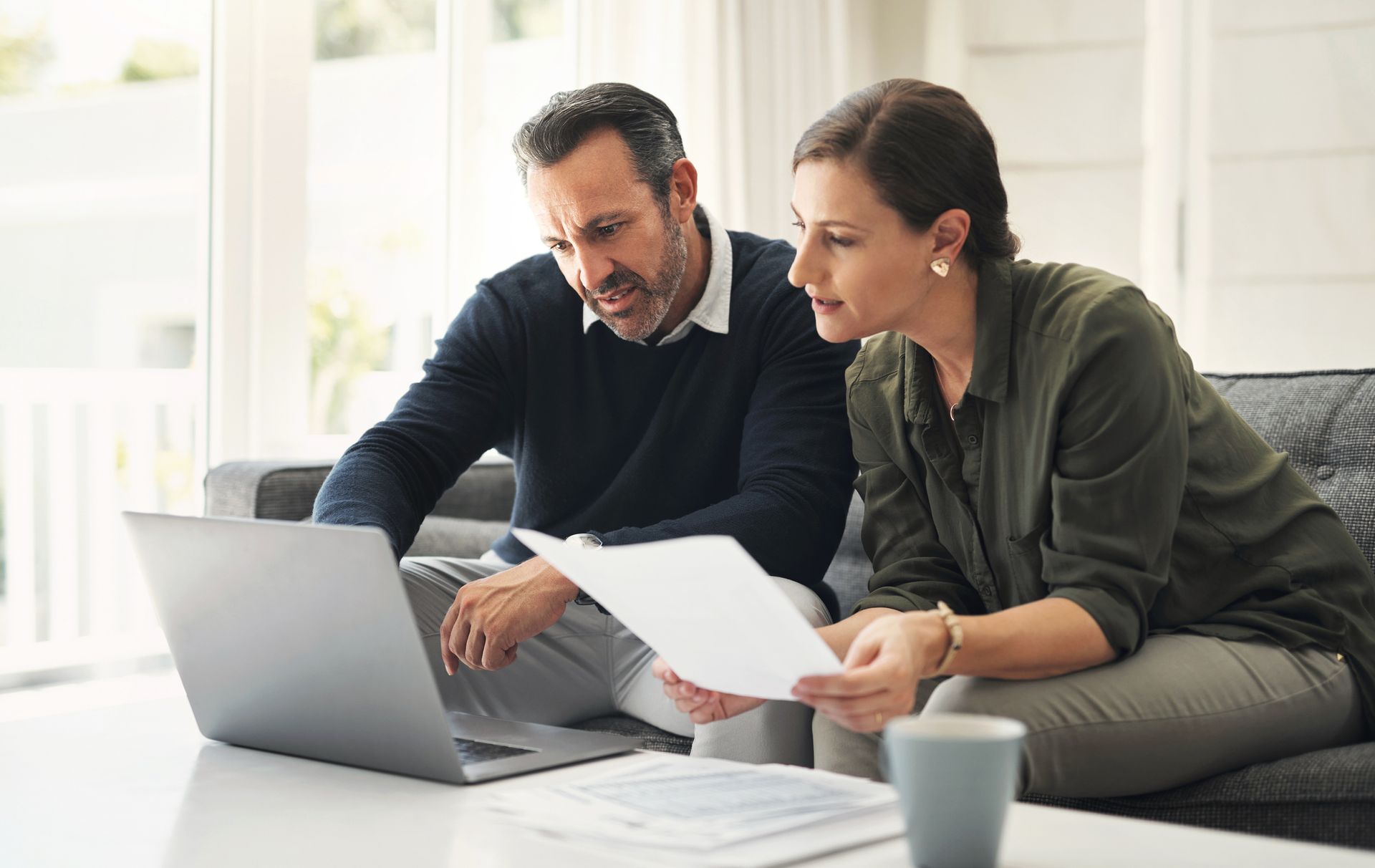 A man and a woman are sitting on a couch looking at a laptop.