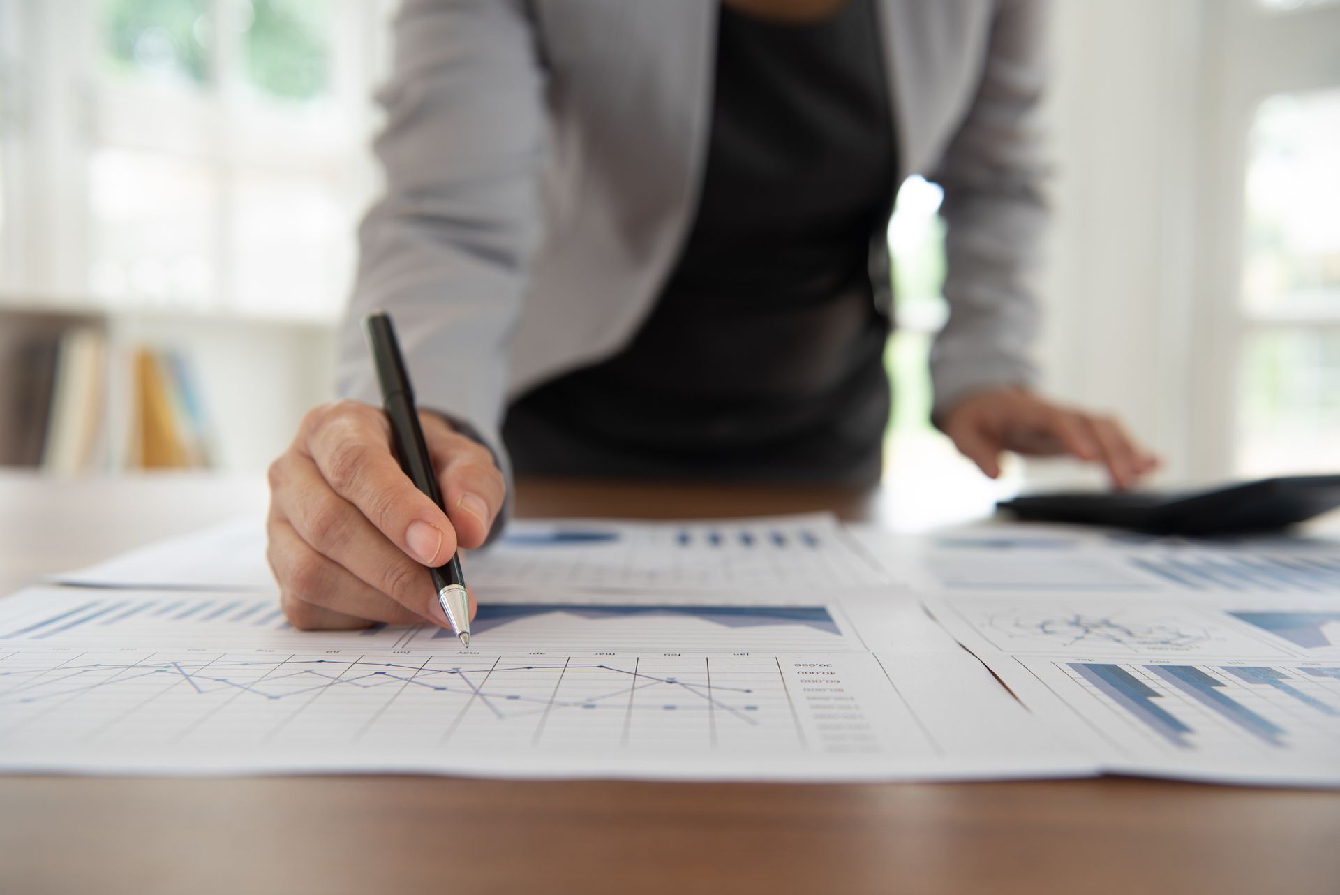 A woman is writing on a piece of paper while using a calculator.